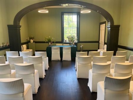 A large bright room with windows to two sides, with green walls and a dark wood floor.