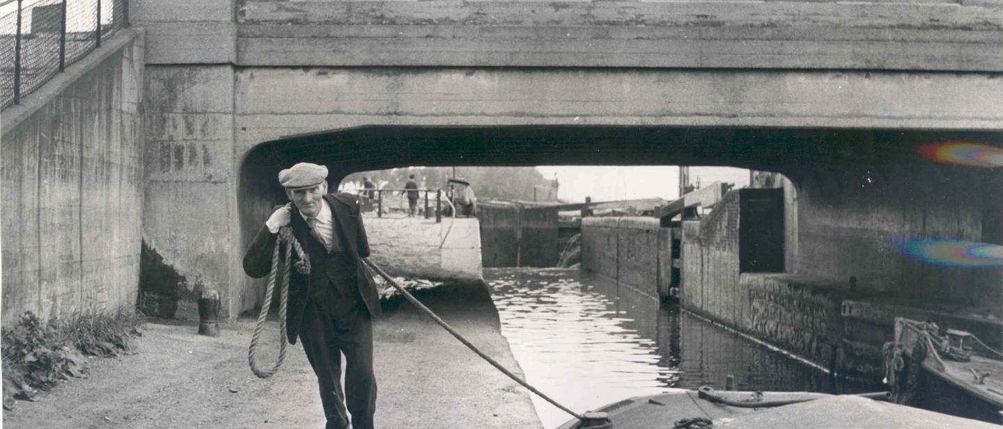 Man from 1950s on towpath dragging a canal boat along with a rope
