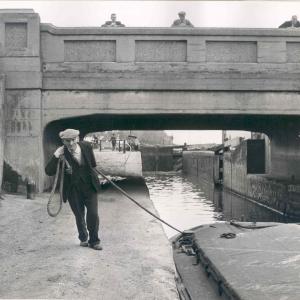 Man from 1950s on towpath dragging a canal boat along with a rope